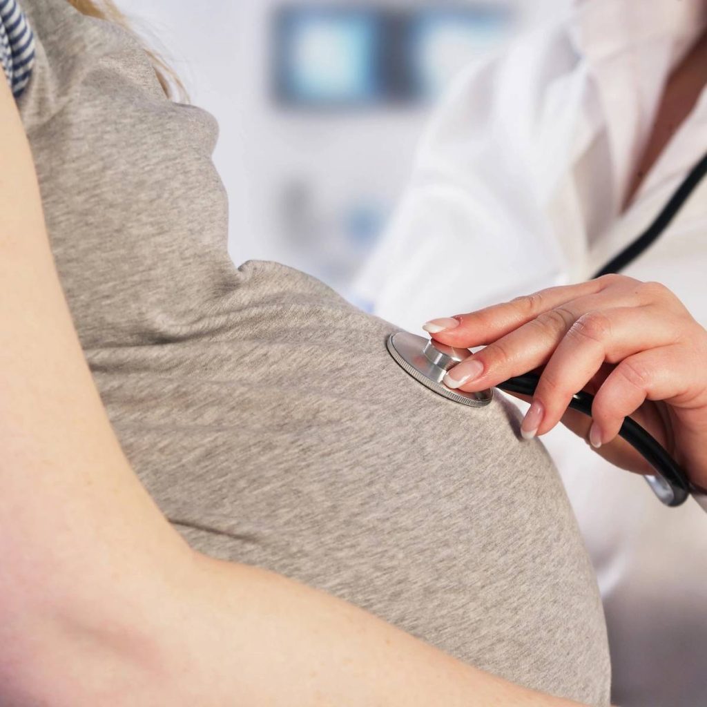 This is a picture of a woman having her pregnant stomach listened to by a stethoscope. 